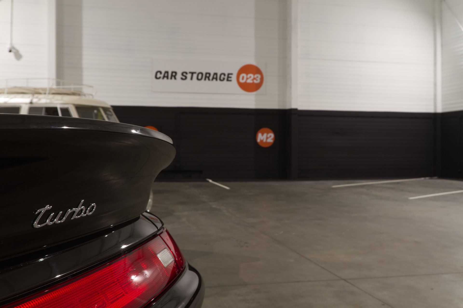 Achterkant van een zwarte Porsche 911 Turbo in de stalling, met het Car Storage 023-logo op de muur